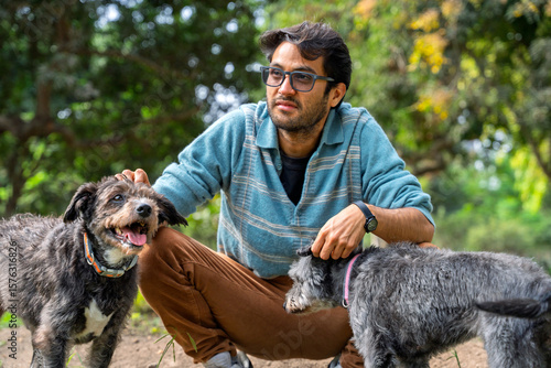 Canvas Print Young man petting two mixed breed dogs in park
