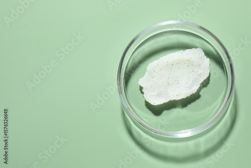 Cosmetic product in Petri dish on green background, top view. Space for text