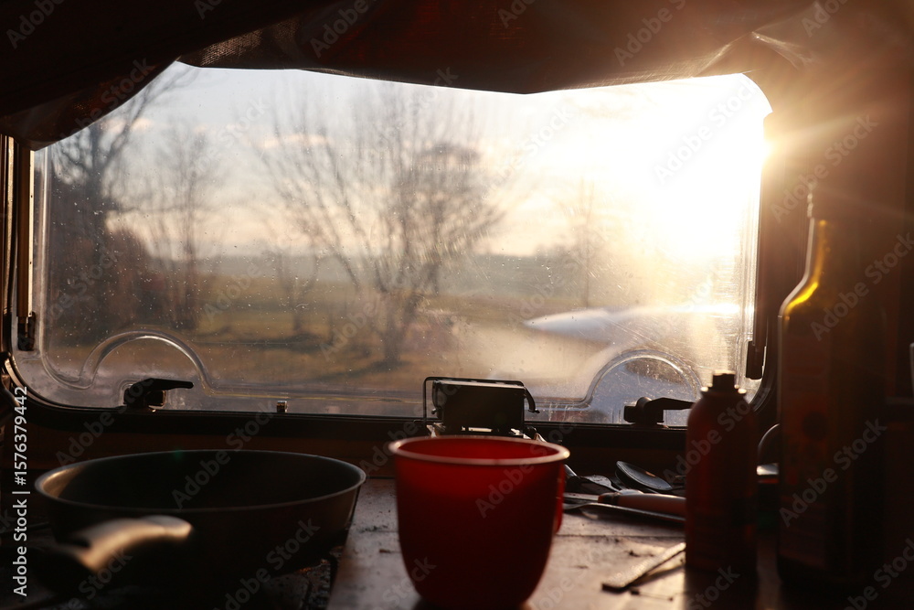 Fototapeta premium A window in a camper van with a pan on the stove and a cup of coffee