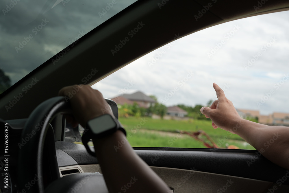 Fototapeta premium Close-up of the man's hand holding the steering wheel and looking for the fields and sunset, summer time and road trip for family leisure time.
