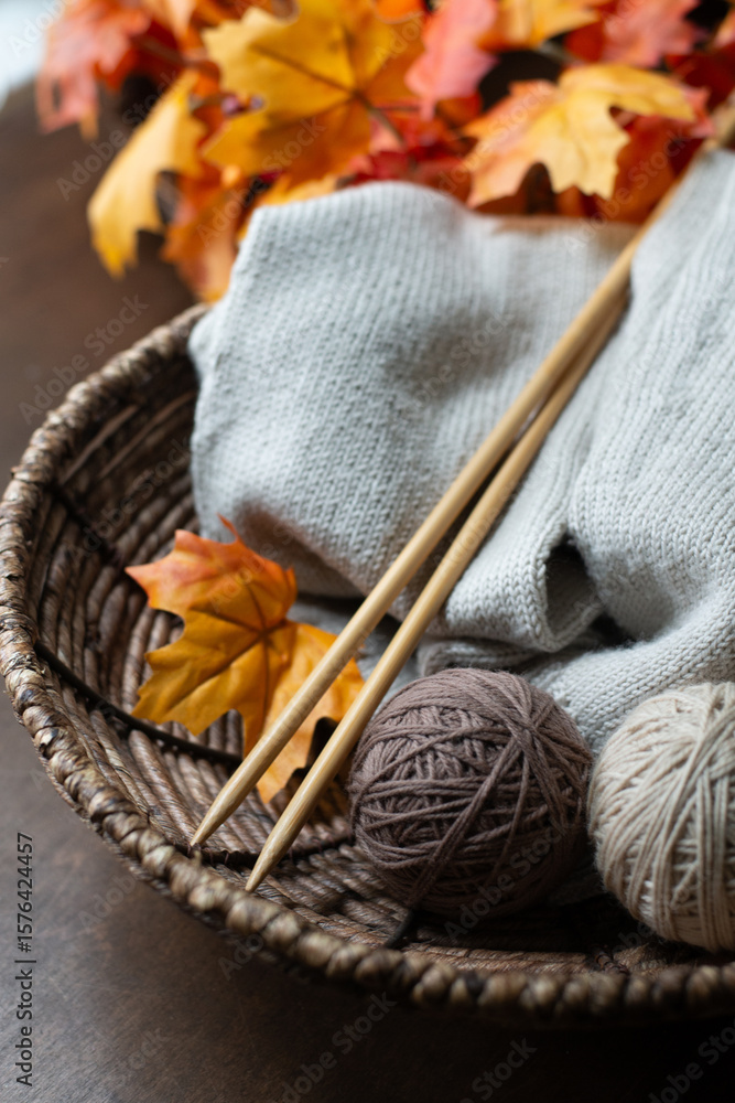 Fototapeta premium Close-Up of Knitting Needles and Yarn with Fall Leaves – Vertical Cozy Detail Shot