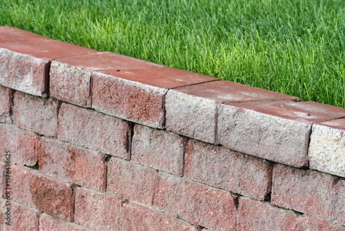 Foto Red cinder paver retaining wall. Bright green grass on top.