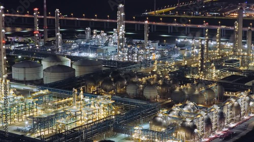 Complex oil refinery and petrochemical plant with illuminated pipes and storage tanks at night near a highway.