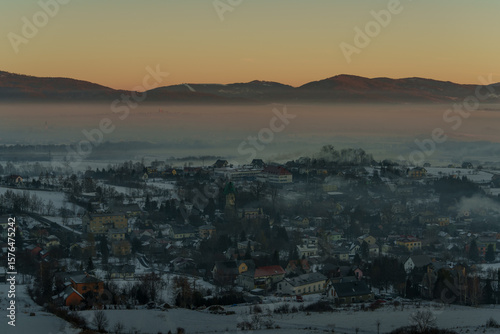 Winter mountain valley with village covered in smog at sunrise