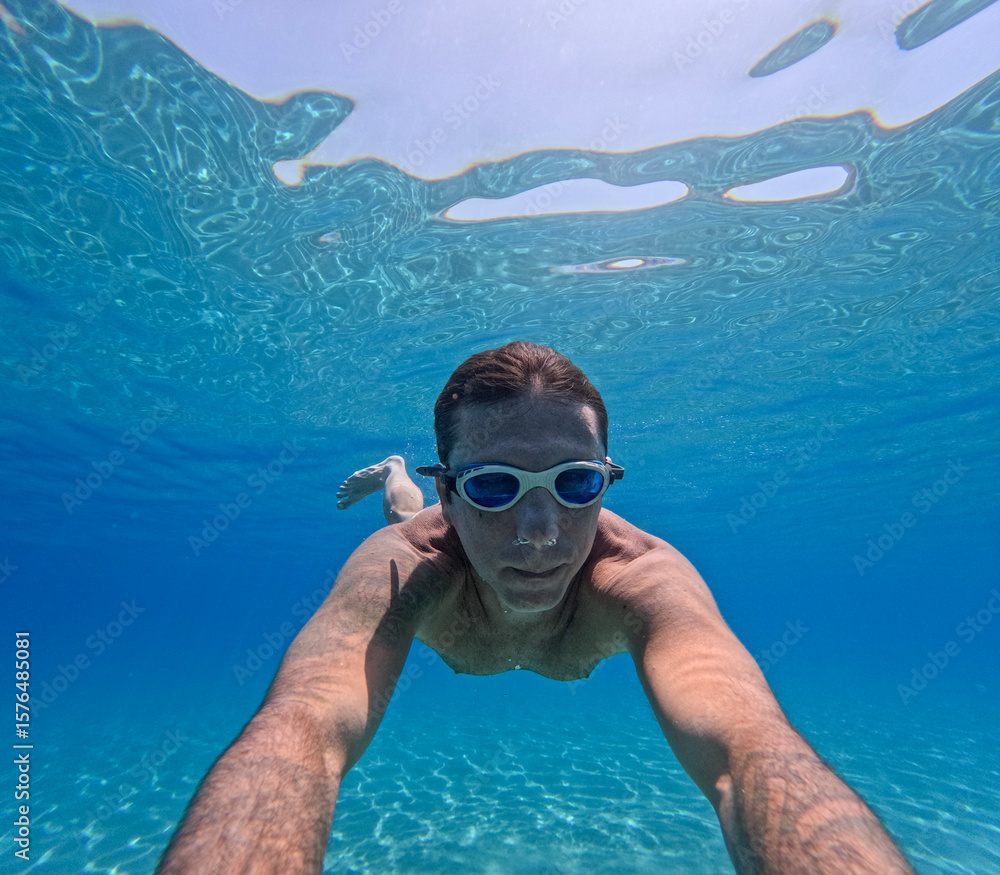 Fototapeta premium Man swimming underwater in the Mediterranean sea off the Sicilian coast. The man is forty years old, of caucasian origin and has swimming goggles on his face