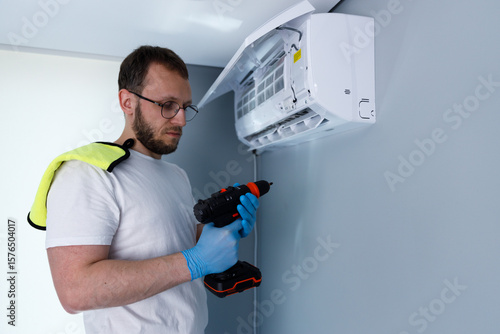 Man Performing Air Conditioner Installation or Repairs with a Power Drill and Wearing Protective Gear on His Hands and Shoulders for Safety and Hygiene in a Modern Indoor Environment