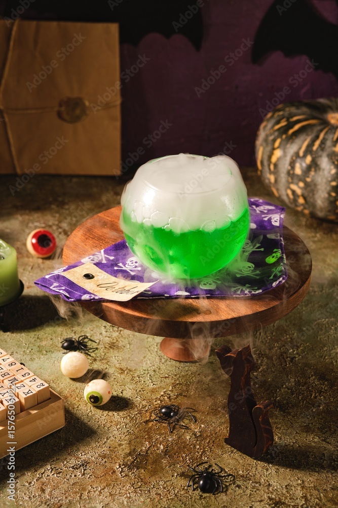 Fototapeta premium Halloween concept, boiling magical green potion in round glass pot with white smoke on wooden stand