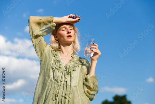 A Woman Relishing the Sunshine While Hydrating on a Warm Day: The Perfect Combination of Refreshment and Relaxation Under a Bright Blue Sky