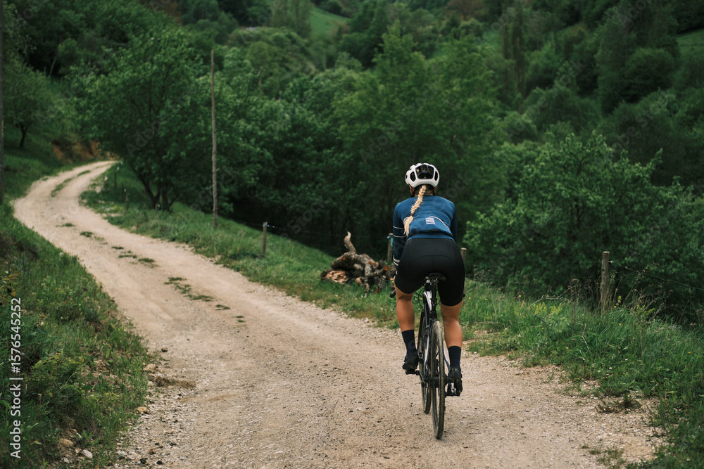 Obraz premium Female cyclist rides gravel bike down scenic country road. Stunning natural landscape. Perfect for travel, adventure, and active lifestyle concepts.