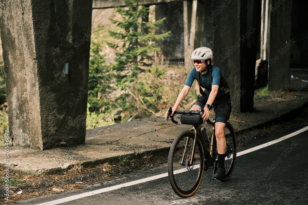 Obraz premium Smiling woman cycling on a gravel bike under a bridge. Adventure, freedom, and outdoor activity. Perfect for travel, sports, and lifestyle imagery.