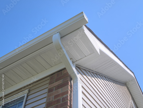 White gutter guard system, fascia, drip edge, soffit, and downspout strap with horizontal vinyl siding at an upscale single-family home neighborhood. 
