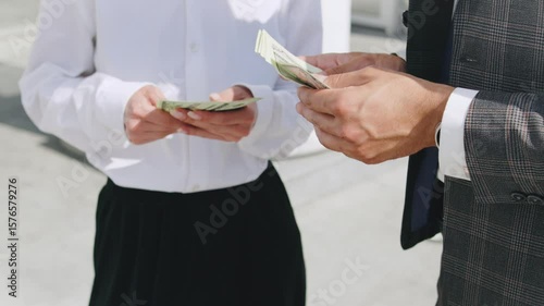 Business transaction between two individuals exchanging cash outdoors in a professional setting during daylight hours