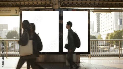 Blurred commuters walk past two blank billboards at a train station platform