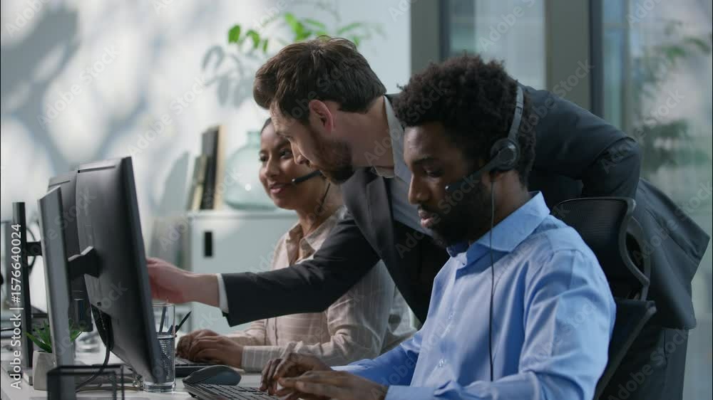 Multiethnic callcenter smiling Caucasian boss explain pointing pc monitor Indian woman employee office teamwork business call center customer support training African man headset helpline hotline desk