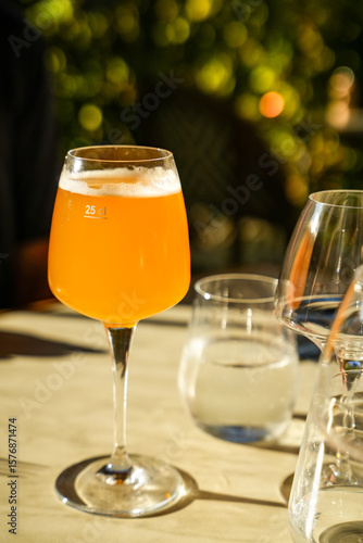 A close-up of a glass of beer illuminated by the sun. Restaurant table set outdoors. Beautiful bokeh background