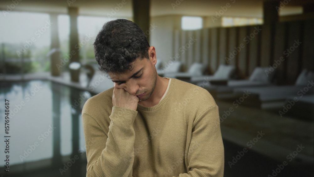 Naklejka premium Man rests hand while yawning in spa lounge beside male hispanic young guest at swimming pool feeling tired.