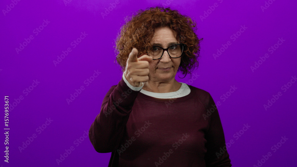 Obraz premium Middle-aged hispanic woman wearing glasses points to head against vibrant purple backdrop, conveying thoughtfulness and creativity.