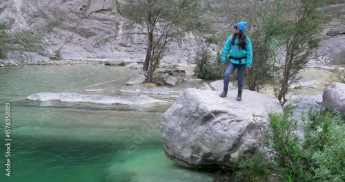 Wide shot of mexican woman that stays over a rock by a pond of blue water