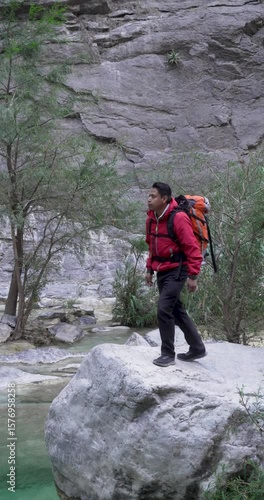 Mexican young explorer walks over a rock by a pond and take a photo