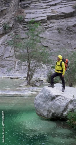 Wide shot of a mexican man in yellow stays over a rock by a water pool