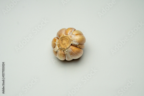 One whole unpeeled garlic clove, viewed from the bottom with its base still attached, placed on a clean white background. Perfect for food photography and cooking ingredient shots.