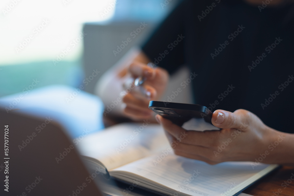 Fototapeta premium Closeup, business woman using mobile phone during remote working on laptop computer at coffee shop. Freelancer, entrepreneur using smartphone, online working. Student studying online, e-learning