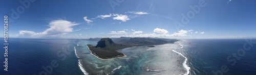 Aerial view of Le Morne Brabant's dark, verdant slopes meet the turquoise embrace of the Indian Ocean under a vast, cerulean sky, Tamarin, RiviÃ¨re Noire District, Mauritius.