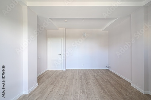 Bright, empty room with light wood floors, white walls, and a white door. Modern, minimalist design