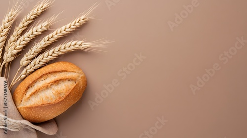 Freshly baked golden bread roll with several wheat ears and linen cloth on a warm brown background