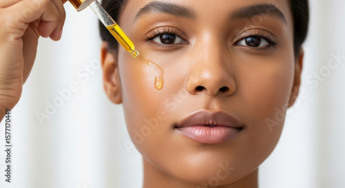 A womans face as a dropper applies serum to her cheek