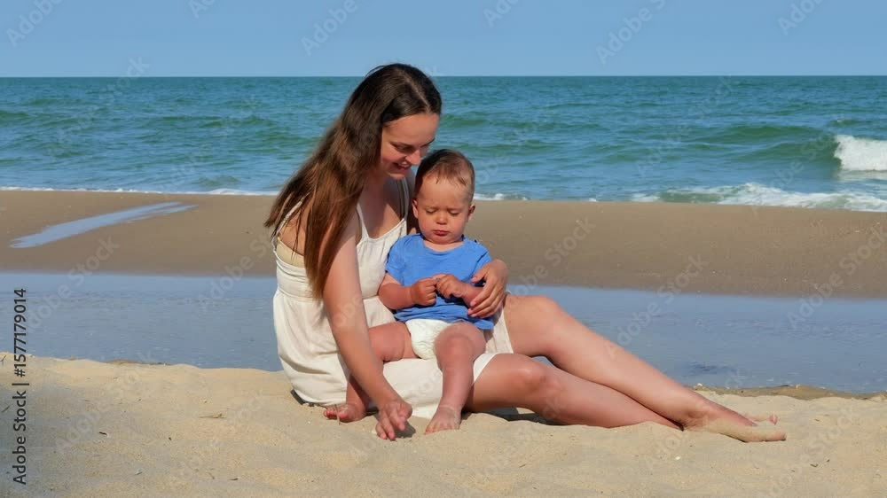 A loving mother in a white dress sits on a sandy beach, gently showing her baby a handful of sand, with the ocean waves in the background. A loving mother in a white dress sits on a sandy beach, gently showing her baby a handful of sand, with the ocean waves in the background.