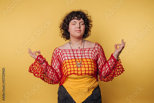 young woman practicing mindfulness through meditation in a colorful ensemble, reflecting a serene emotional state on yellow background