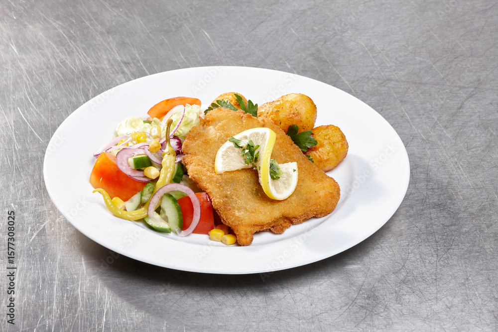 A delicious plate features crispy fried fish garnished with lemon, accompanied by a vibrant salad of fresh vegetables and fried potatoes, showcasing a hearty meal A delicious plate features crispy fried fish garnished with lemon, accompanied by a vibrant salad of fresh vegetables and fried potatoes, showcasing a hearty meal