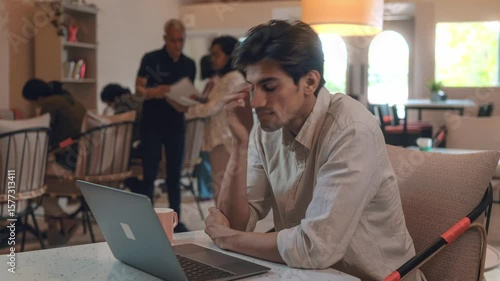 Timelapse of young male corporate office employee or freelancer interacting with colleagues or associates while busy working on a laptop, sipping coffee in a modern business open workplace or cafe