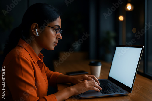 Serious woman working on laptop at night with glasses and moody light in warm office setting