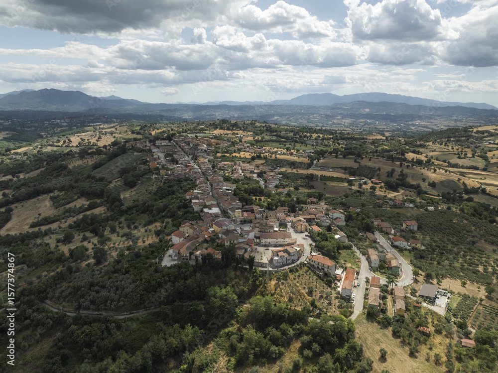 Aerial view of a tranquil town nestled among rolling hills under a vast sky, with verdant trees contrasting with the terracotta roofs, Bonito, Avellino, Italy. Aerial view of a tranquil town nestled among rolling hills under a vast sky, with verdant trees contrasting with the terracotta roofs, Bonito, Avellino, Italy.