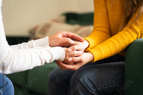One woman holding another woman hand during a heartfelt conversation in living room background, two girls holding hands in symbol of female friendship, comfort and support between friends, close-up