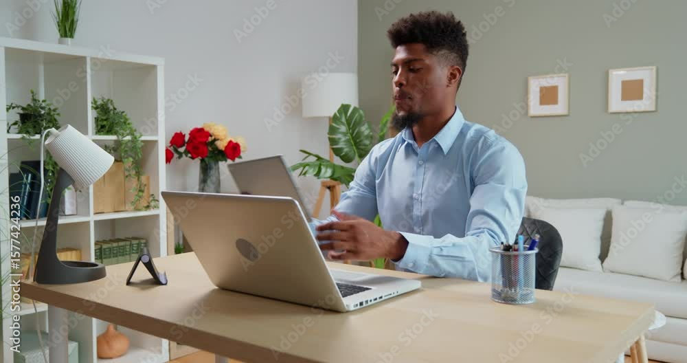 Smiling young african american man using laptop and digital tablet while working remotely from home Smiling young african american man using laptop and digital tablet while working remotely from home