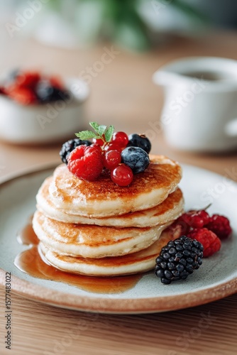 Delicious stack of fluffy pancakes topped with fresh berries and syrup served on a wooden table