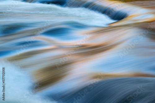 Abstract landscape of a Bond Falls rapids captured with motion blur and illuminated by reflected color from sunlit autumn maples and blue sky overhead, Michigan's Upper Peninsula, USA