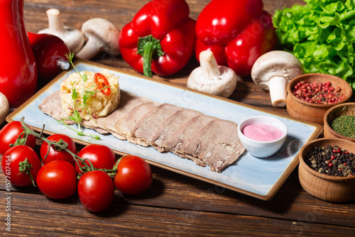 The photo shows a blue rectangular plate with several slices of smoked or cured meat topped with a small portion of a creamy salad or coleslaw garnished with microgreens and red chili slices