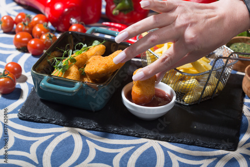 The photo shows a black slate serving board with a small teal dish containing several breaded chicken nuggets, garnished with microgreens. 