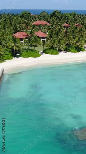 high-altitude, wide-angle drone video slowly sweeping over a luxurious tropical island resort, brilliant clear sunlight illuminating elegant buildings, verdant palms, transparent sand beach, and