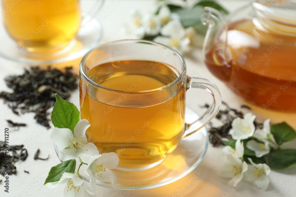 Aromatic jasmine tea in glass cup, teapot, flowers and dried leaves on white table, closeup Aromatic jasmine tea in glass cup, teapot, flowers and dried leaves on white table, closeup