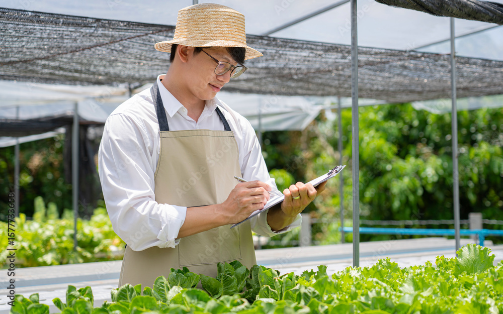 Obraz premium A man wearing a hat and apron is writing on a clipboard in a greenhouse