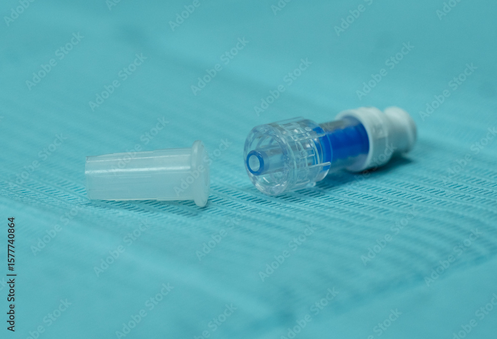 Naklejka premium Close-up rear view of a non-return injection cap with its protective cover placed nearby. Medical connector component used in IV therapy, port-a-cath systems, and catheter sealing.