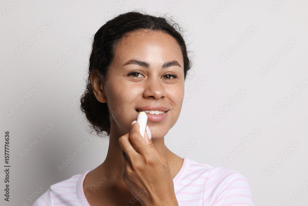 Smiling woman applying lip balm onto her lips on grey background Smiling woman applying lip balm onto her lips on grey background