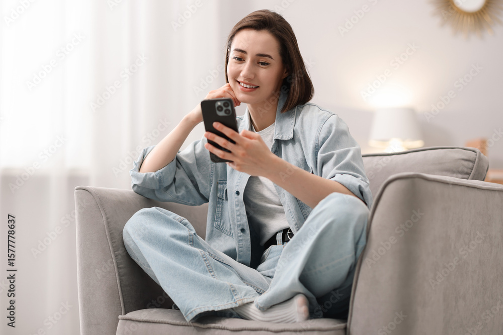 Obraz premium Woman using modern smartphone in armchair at home