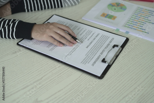 A real estate woman agent is reading and checking paper documents, signing the lease agreement, preparing contract and terms and conditions details and checking data analysis as a remote freelancer.