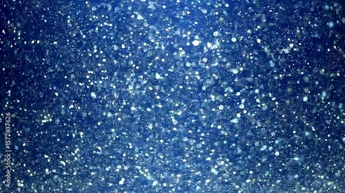 Falling snowflakes and shiny ice crystals drift across a blue winter sky, evoking holiday warmth and seasonal charm